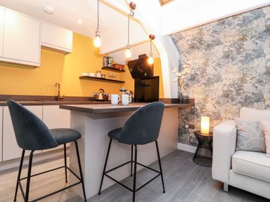 A kitchen area with bar stools and pendant lights next to a sofa and a side table with a lamp at Fenty's in Bowness-On-Windermere