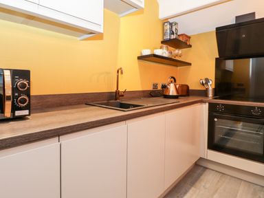 A kitchen with a microwave a sink kettle toaster utensils an oven and open shelves with cups and jars at Fenty's in Bowness-On-Windermere