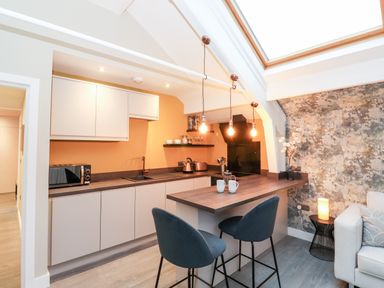 A kitchen with white cabinets a wooden countertop two blue chairs hanging light bulbs and a skylight at Fenty's in Bowness-On-Windermere