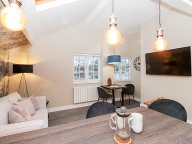 A living room with a sofa cushions a floor lamp a dining table two chairs a wall clock and a mounted TV at Fenty's Bowness-On-Windermere