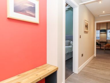 A hallway with wooden bench and framed pictures leading to a bedroom and dining area at Fenty's in Bowness-On-Windermere