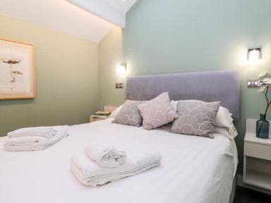 A bedroom with a bed with white linens and folded towels on top and pillows against a lavender headboard at Fenty's in Bowness-On-Windermere