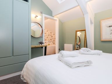 A bedroom with a bed with folded towels and an open door showing a bathroom with animal wallpaper at Fenty's in Bowness-On-Windermere