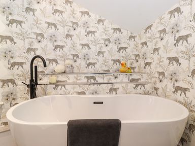 A bathroom with a white freestanding bathtub black faucet and animal patterned wallpaper at Fenty's Bowness-On-Windermere