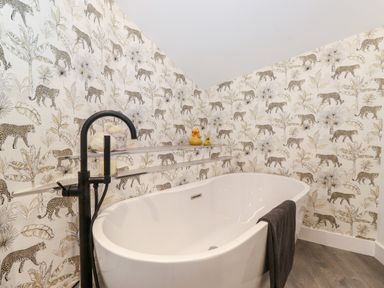 A bathroom with a white freestanding bathtub a black faucet and leopard print wallpaper at Fentys in Bowness-On-Windermere