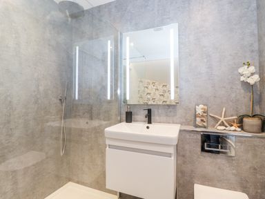 A bathroom with a shower area a sink with a cabinet a mirror with lights and decorative items on a shelf at Fenty's in Bowness-On-Windermere