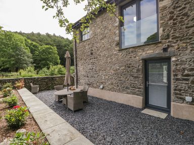 An outdoor seating area with a stone wall and patio furniture next to a stone house at Bank Hurst Coach House in Ulverston