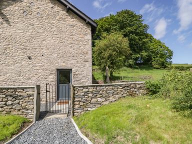 Stone house wall with a door and a small gate leading to a gravel path in a garden at Bank Hurst Coach House in Ulverston