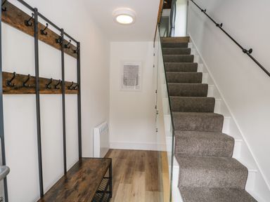 A hallway with a carpeted staircase and wooden bench with coat hooks at Bank Hurst Coach House in Ulverston