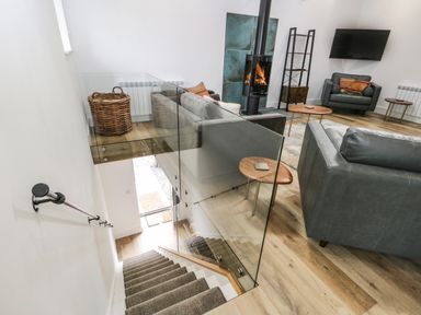 A living room with a wood stove tv armchairs and sofas viewed from a stairway at Bank Hurst Coach House in Ulverston