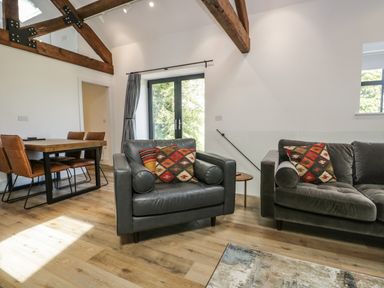 A living room with two gray armchairs with patterned cushions and a dining table with brown chairs at Bank Hurst Coach House in Ulverston