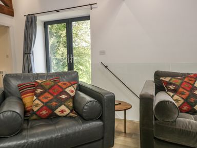 Two black leather chairs with patterned cushions near a glass door and a wooden side table at Bank Hurst Coach House in Ulverston