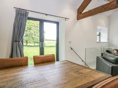 Dining area with wooden table and leather chairs near glass doors with view of green field at Bank Hurst Coach House in Ulverston
