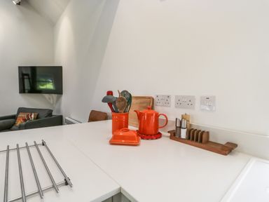 A kitchen counter with utensils in a red holder a red teapot a butter dish and a wooden tray with salt and pepper shakers in a living area at Bank Hurst Coach House Ulverston