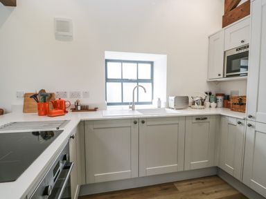 A kitchen with a window above the sink white countertops gray cabinets and kitchen appliances at Bank Hurst Coach House in Ulverston