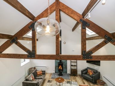 A living room with wooden beams a hanging light a fireplace sofas and a coffee table at Bank Hurst Coach House in Ulverston