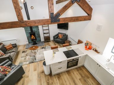 An open plan living area with a kitchen island bar stools a sofa and armchairs a fireplace and exposed wooden beams at Bank Hurst Coach House in Ulverston