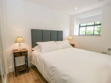 A bedroom with a bed with white bedding two bedside tables with lamps and a window at Bank Hurst Coach House in Ulverston