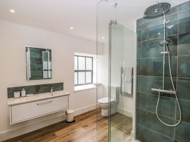A bathroom with a sink, mirror, toilet, shower with glass partition, towel rack, and window at Bank Hurst Coach House in Ulverston