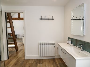 A bathroom with a sink cabinet mirror a radiator and wooden floor at Bank Hurst Coach House in Ulverston