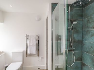 A bathroom with a toilet a towel rack with white towels and a shower with blue tiles and glass door at Bank Hurst Coach House in Ulverston