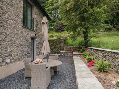 An outdoor patio area with a round table and four chairs with an umbrella next to a stone building at Bank Hurst Coach House in Ulverston