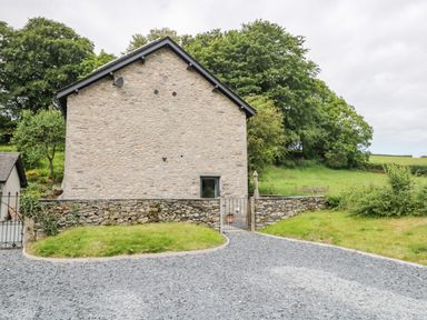 A stone house with a gravel driveway grass patches and trees at Bank Hurst Coach House in Ulverston