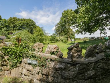 A stone wall with ivy and a sign reading Bank Hurst with trees and grass behind at Bank Hurst Coach House in Ulverston