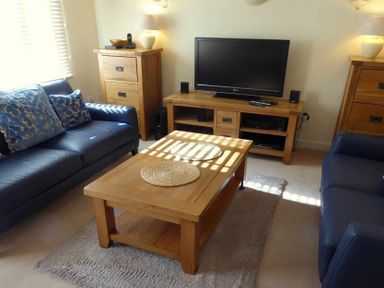 A living room with two dark blue sofas a wooden coffee table a TV on a wooden stand and wooden cabinets at House on the Green in Chipping Norton