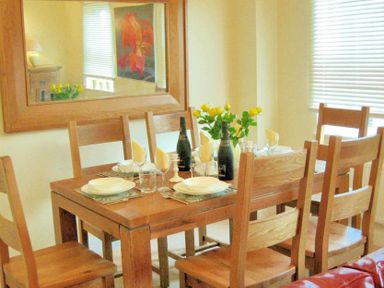A dining table set with plates glasses napkins and bottles surrounded by wooden chairs at House on the Green Chipping Norton