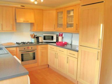A kitchen with wooden cabinets a gas stove an oven a microwave and a refrigerator at House on the Green in Chipping Norton