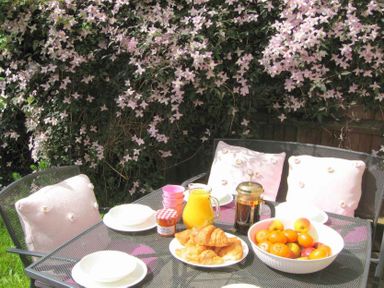 A garden table set with croissants orange juice coffee fruit and cushions on chairs at House on the Green in Chipping Norton