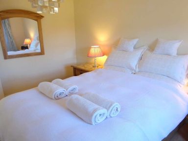 A bedroom with a double bed four rolled towels bedside table lamp and a mirror on the wall at House on the Green in Chipping Norton