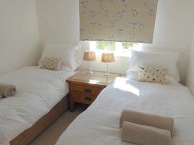 A bedroom with two single beds with white bedding and a wooden nightstand with two lamps at House on the Green in Chipping Norton