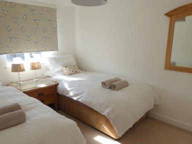 A bedroom with two single beds a wooden nightstand with two lamps and a mirror on the wall at House on the Green in Chipping Norton