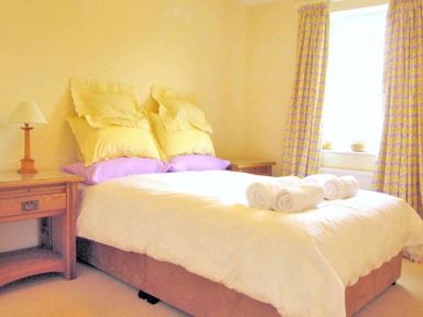A bedroom with a double bed side tables a lamp and a window with curtains at House on the Green in Chipping Norton
