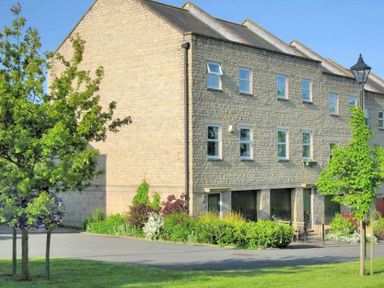 A stone residential building with multiple windows and bushes in front with a street lamp and trees at House on the Green in Chipping Norton