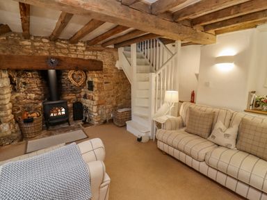 A living room with a stone fireplace a wood stove two sofas a white staircase and a lamp at Chippy Cottage in Chipping Norton