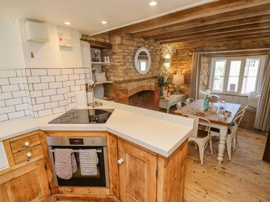 A kitchen area with wooden cabinets and an oven adjoining a dining area with a wooden table and metal chairs at Chippy Cottage in Chipping Norton