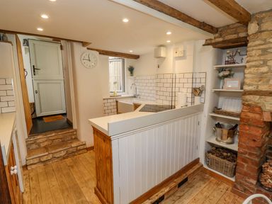 A kitchen with wooden floors a white countertop a farmhouse sink and shelves with decorations at Chippy Cottage in Chipping Norton