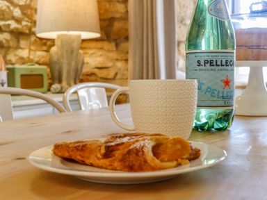A wooden table with a white textured mug a plate with pastries and a bottle of sparkling water in a kitchen