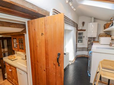 A narrow kitchen area with wooden cabinets a countertop appliances and an open wooden door at Chippy Cottage in Chipping Norton