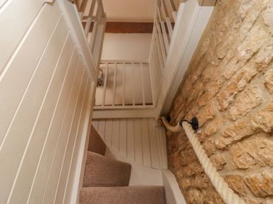A staircase with carpeted steps a rope handrail on a stone wall and white wooden banisters at Chippy Cottage in Chipping Norton
