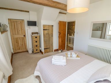A bedroom with a bed, wooden doors, a small chest of drawers, a wall mirror, and a tray with teapot and cups on the bed at Chippy Cottage in Chipping Norton