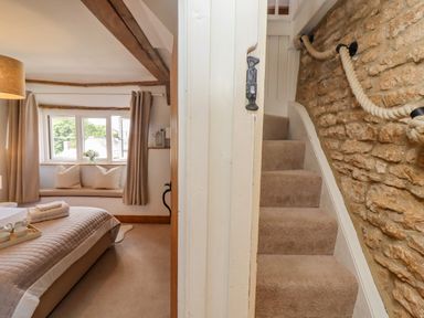 A bedroom with a bed and window seat next to a staircase with rope handrails at Chippy Cottage in Chipping Norton
