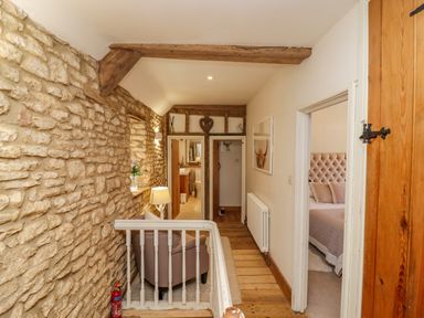 A hallway with a stone wall and wooden floor leading to a bathroom and bedroom at Chippy Cottage in Chipping Norton