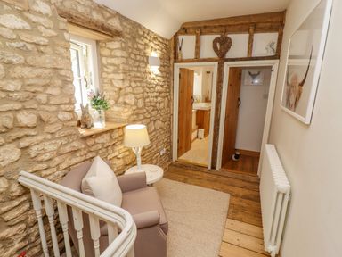 A small sitting area with an armchair a side table and a lamp next to a stone wall with a window and two wooden doors at Chippy Cottage in Chipping Norton