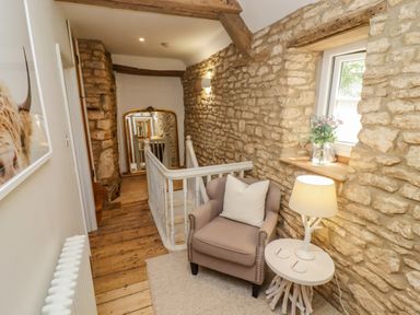A hallway with stone walls wooden floor an armchair a small table with a lamp and a window with flowers at Chippy Cottage in Chipping Norton
