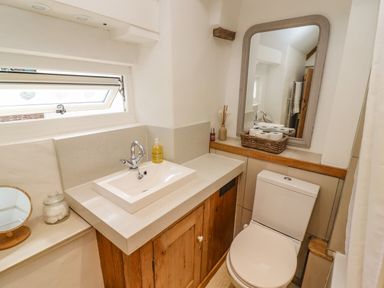 A bathroom with a sink and wooden cabinet a toilet a mirror and a window at Chippy Cottage in Chipping Norton