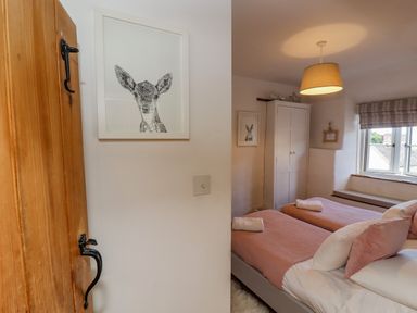 A bedroom with two single beds pink bedding a wooden door and framed animal pictures at Chippy Cottage in Chipping Norton